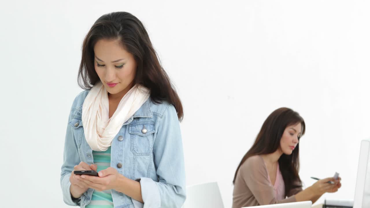 창의적인 사업가 여자가 뒤에 동료와 함께 문자를 보내고 있습니다.