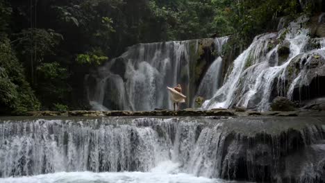 4k video of a woman walking across the rocks to the beautiful, cascading water at piala waterfall in luwuk, sulawesi indonesia
