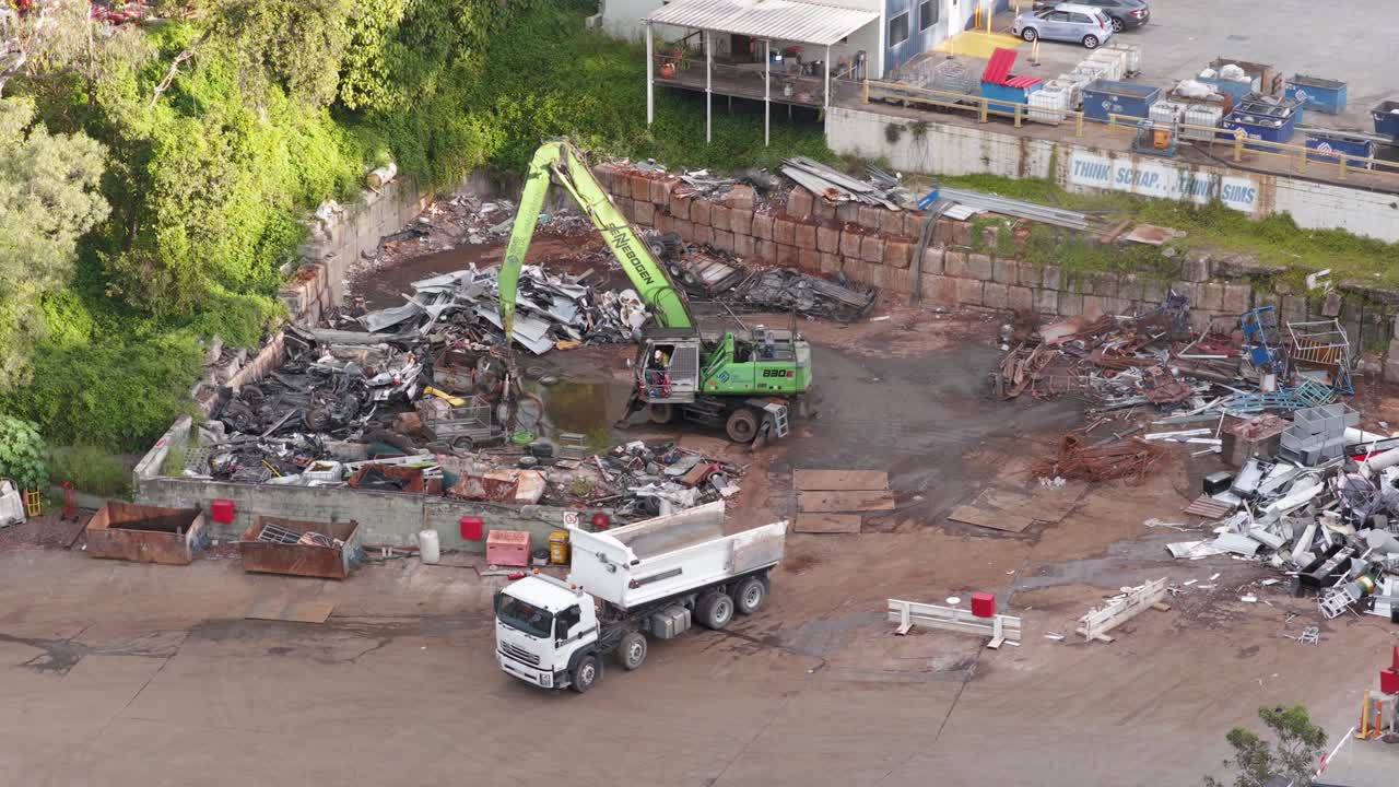 Aerial footage of a truck and machinery moving metal scrap in a Gold Coast junkyard. Bright daylight, dynamic camera angles