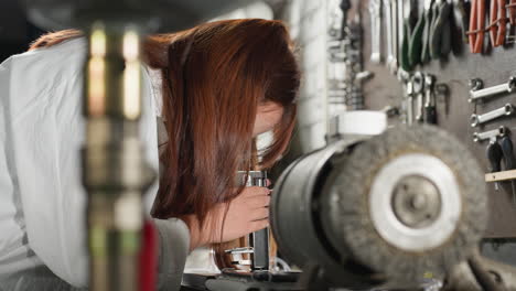 side view of engineer observing a sample under a microscope, adjusting the focus, with hair cascading over her shoulder, in a workshop filled with mechanical tools