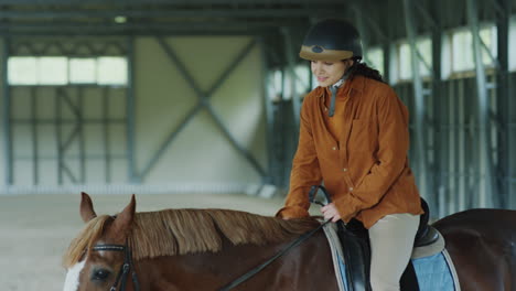 equestrian rider petting her horse in an indoor arena