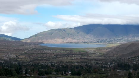 Stunning-aerial-drone-view,-city-with-a-lake-and-a-big-mountain-in-the-background-on-a-cloudy-day,-Argentina,-Tafi-del-Valle