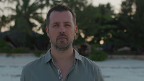 close up front facing shot of a thoughtful man walking alone towards ocean water on the remote tropical beach on the sunset