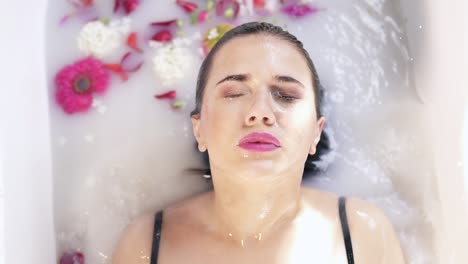 close up view of young woman bathing in milk bath filled with flowers and getting up with her eyes closed. spa and skin care