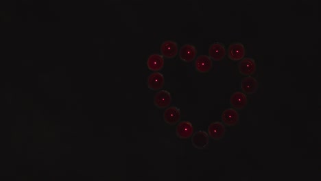 disparo aéreo de velas rojas encendidas en forma de corazón romántico siendo soplado en fondo negro