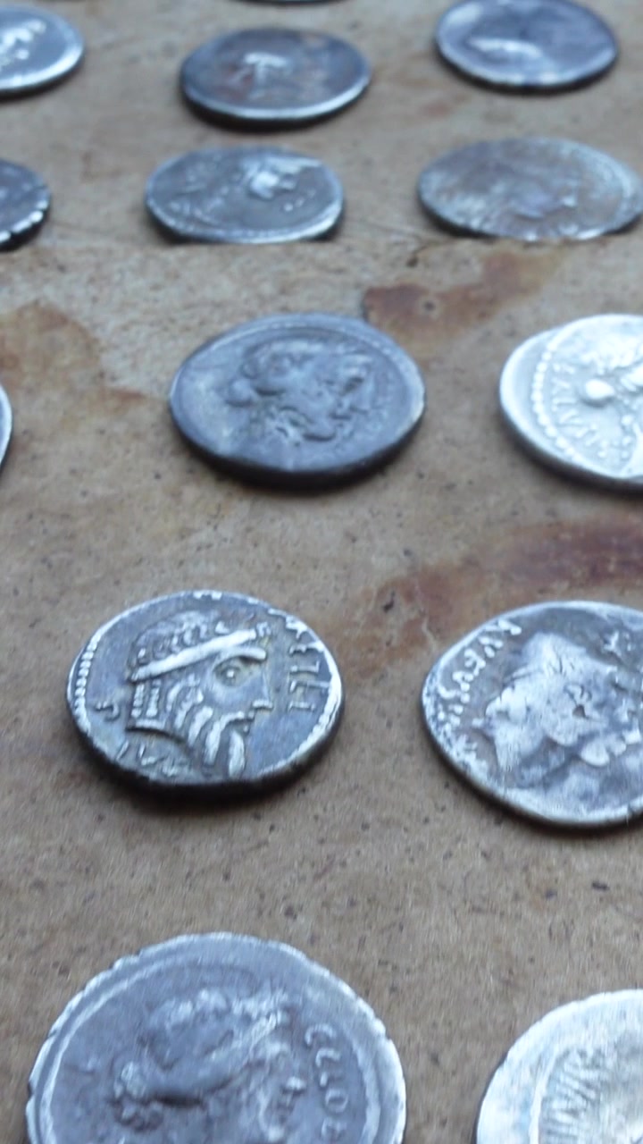Panorámica de monedas romanas de plata de varios emperadores sobre una mesa de madera antigua. Vista vertical.