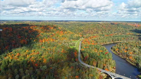 The-captivating-scenery-of-the-autumn-season,-observed-through-an-aerial-perspective-using-a-drone,-showcases-an-idyllic-lake-embellished-with-an-alluring-bridge-and-a-captivating-forest