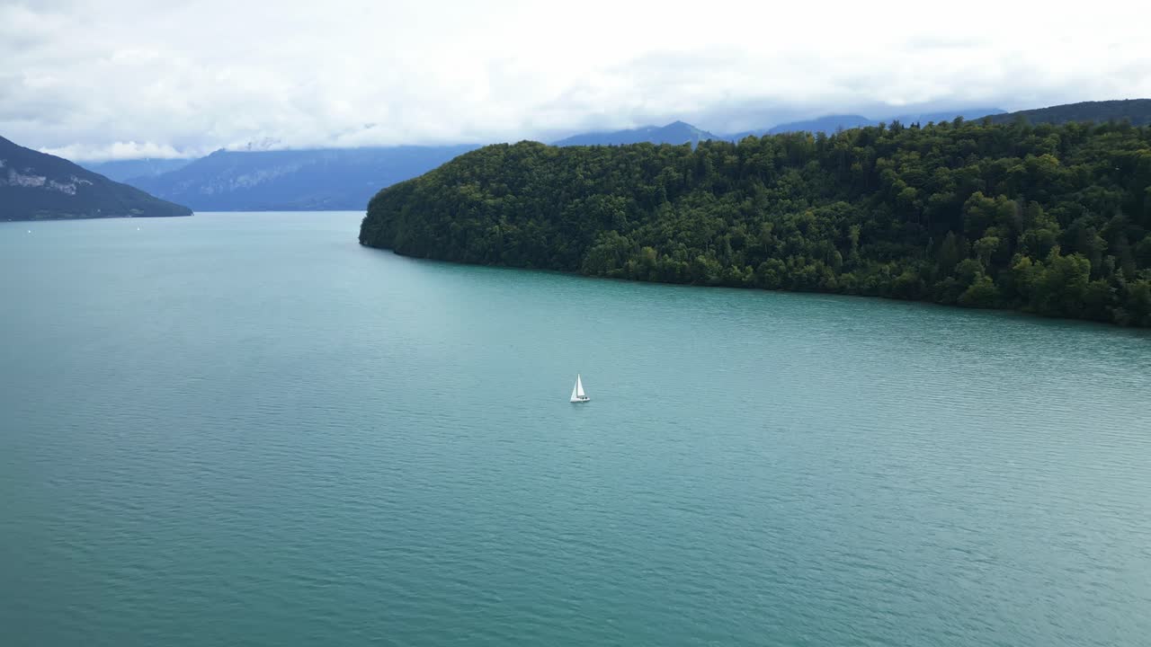 Push in drone shot of the bay above Thun Lake with a white boat sailing in the Canton of Bern in Switzerland.
