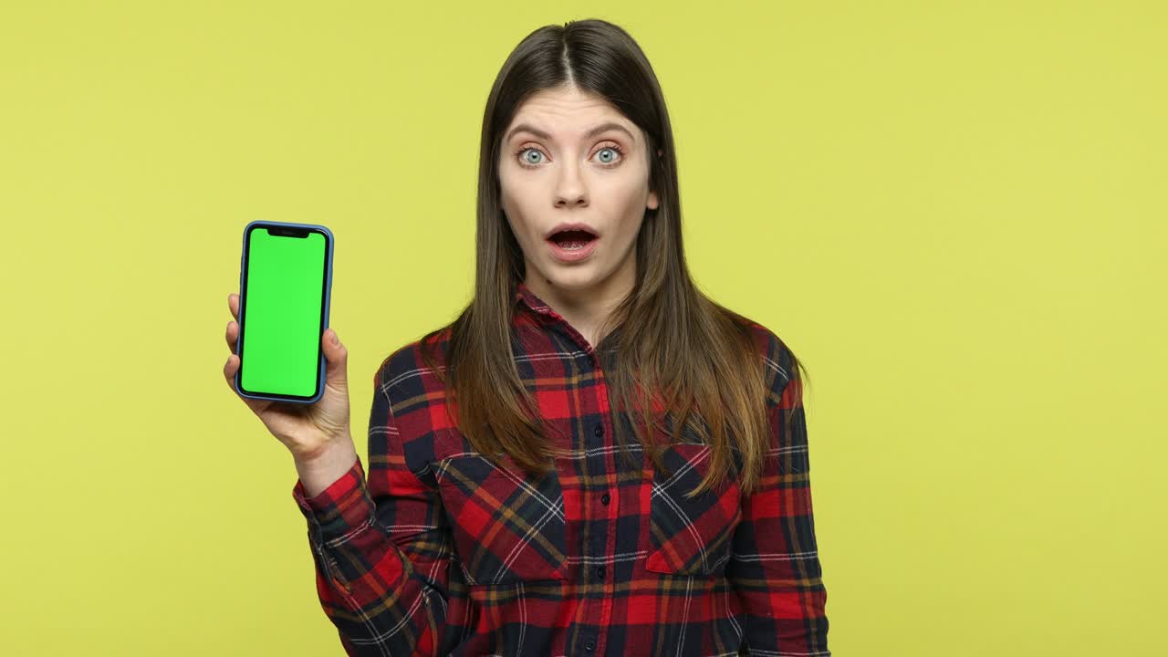 Surprised amazed woman holding and showing smartphone with green screen display