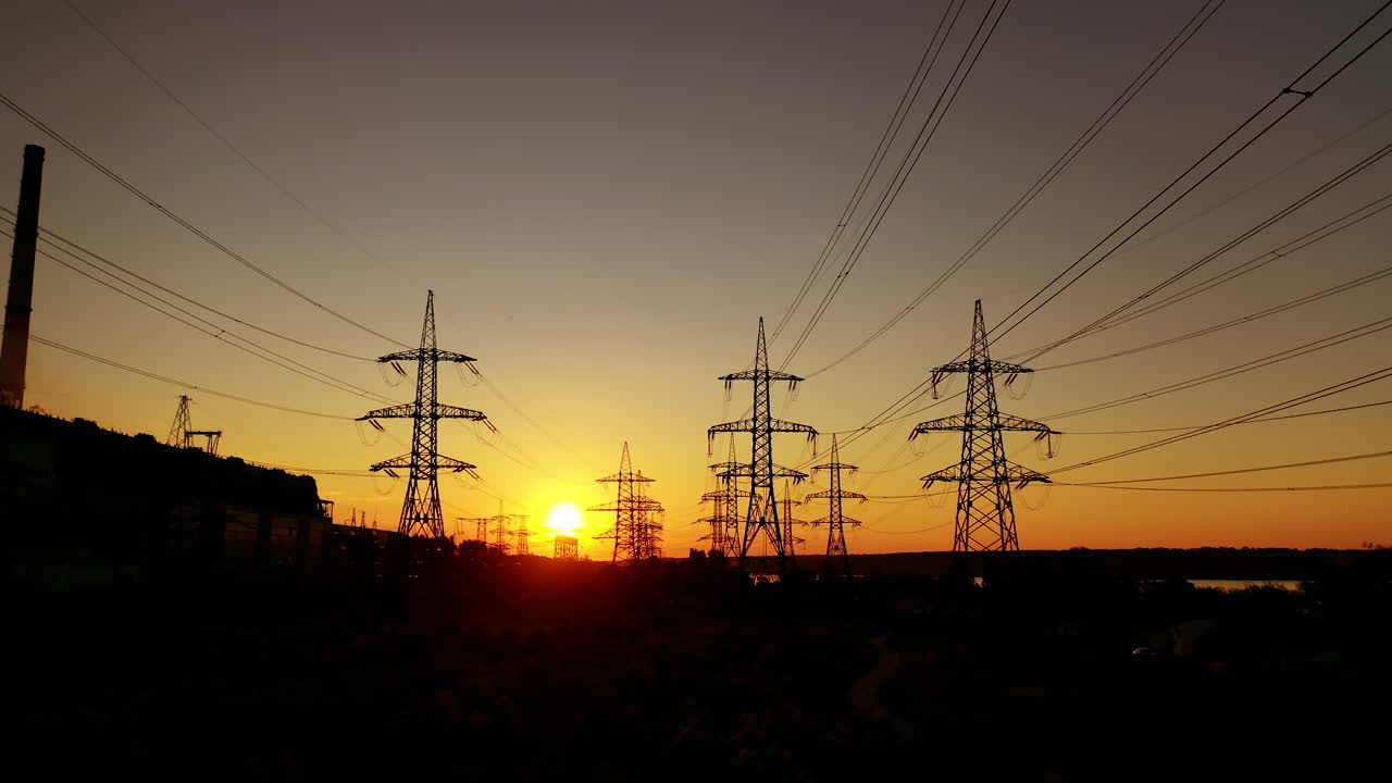 Electric pylons against orange sunset. Dark background of high-voltage electric lines in the evening. Transmission lines on the setting sun.