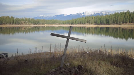 a simple wooden cross on the shore of a beautiful lake in the mountains of montana on a sunny day, slow push in