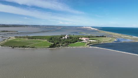 Lagoon-and-Mediterranean-Sea-with-Maguelone-Cathedral-on-a-small-volcanic-island,-Wide-aerial-shot