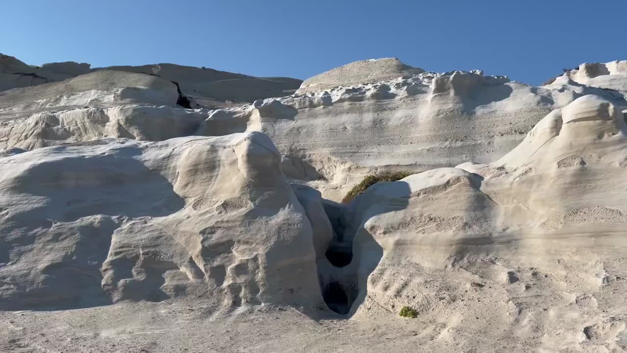 Vibrant cliffs in white, pink, yellow, and red rise above calm turquoise waters of the Aegean Sea under a bright blue sky on Milos Island, Greece.