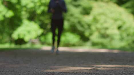 Ground-Level-Shot-Of-Young-Woman-Exercising-Running-Towards-Camera-Into-Focus-In-City-Park-1