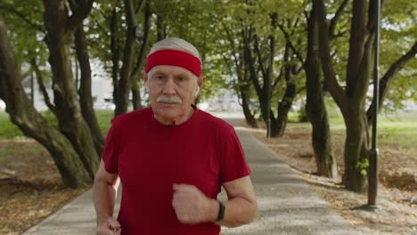 male senior person running along the road in park. mature runner man training, listening music