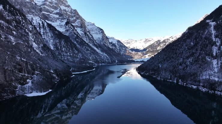 Aerial captures the breathtaking beauty of the Klöntalersee in Switzerland. The lake stretches out like a ribbon between towering, snow-capped mountains.