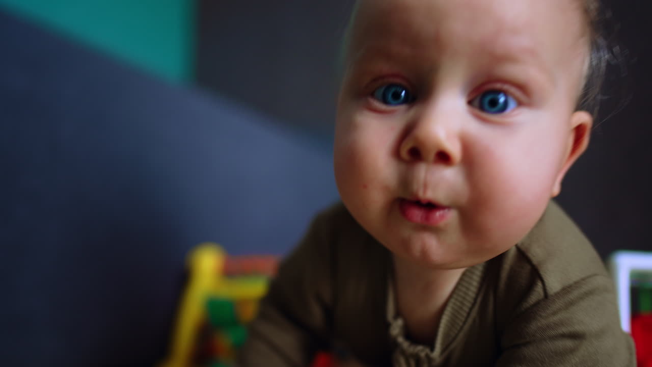 Persistent little baby boy crawls towards camera. Close up. Infant moving by the floor around the toys.