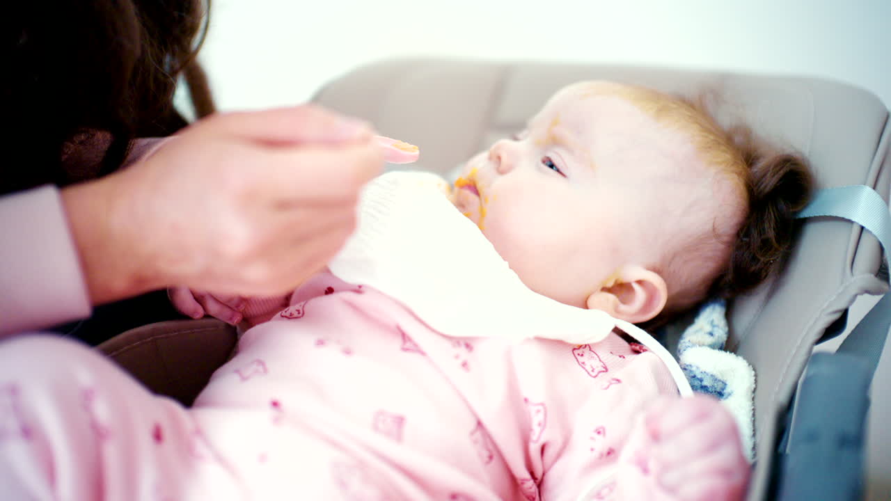 Primo piano di un bambino che viene delicatamente nutrito con un cucchiaio da un adulto.