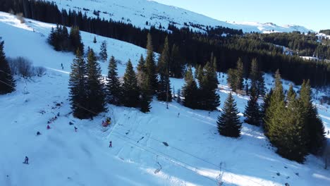 clip aéreo bajo de personas esquiando en una ladera de montaña en la estación de esquí de vitosha cerca de sofía, bulgaria con bosques de coníferas y picos cubiertos de nieve en el fondo