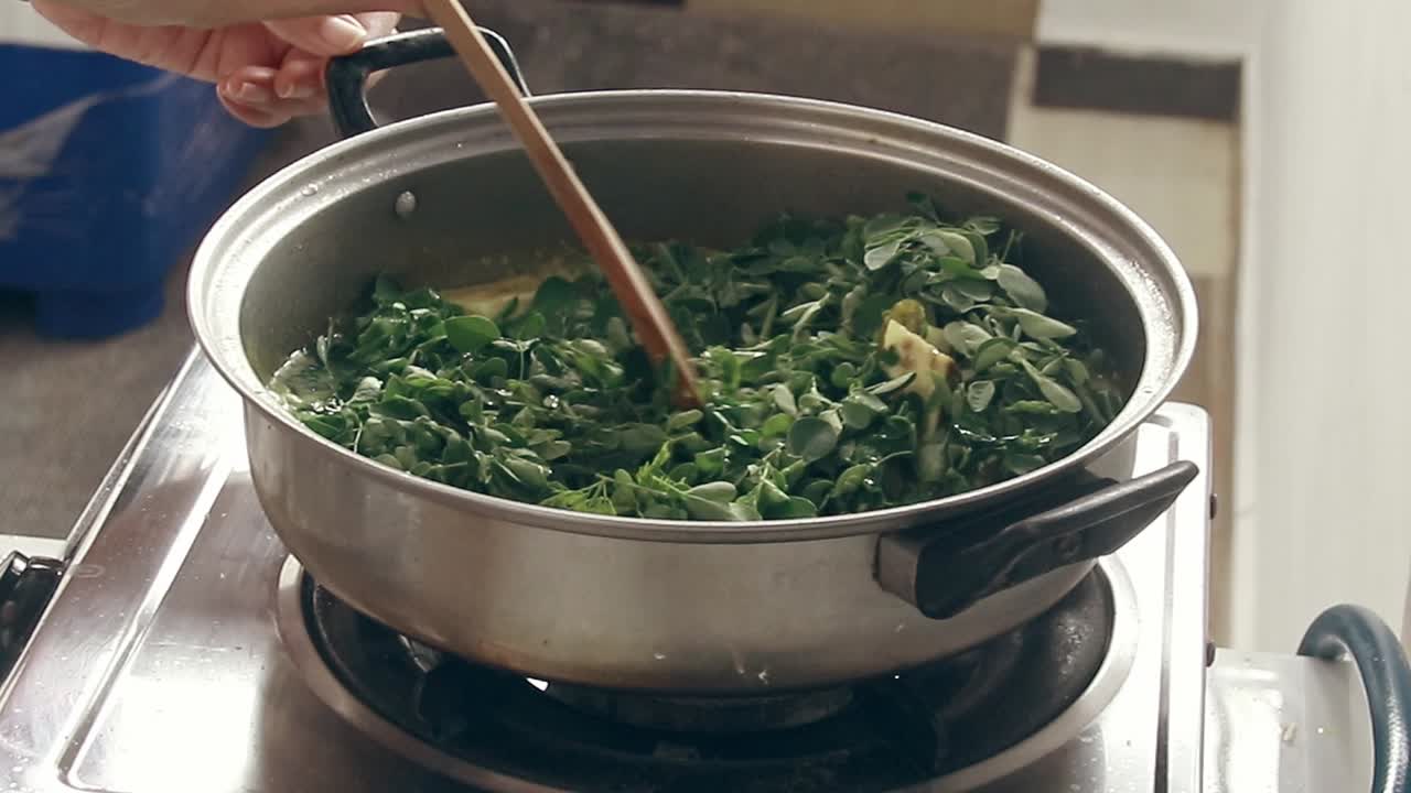 mezclar y agitar hojas de moringa o malunggay para cocinar ginataang gulay o estofado de verduras con leche de coco, un plato tradicional filipino vegano