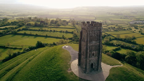 Un-Dron-Disparó-Alrededor-De-Glastonbury-Tor,-Una-Colina-En-Somerset,-Reino-Unido,-El-Disparo-Rodeó-Una-Torre-En-La-Cima-De-La-Colina-Con-Campos-En-El-Fondo