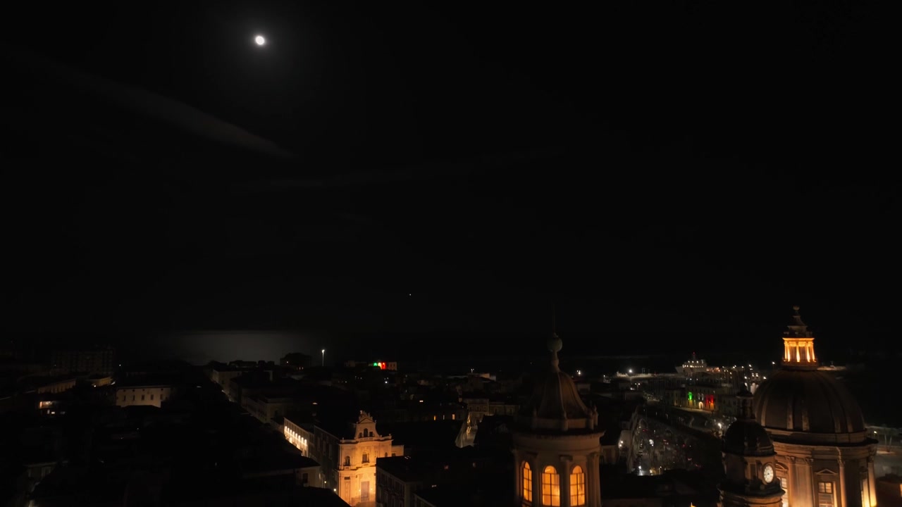 Suggestivo scatto notturno di cattedrali barocche illuminate e tetti della città sotto una luna piena brillante, che cattura l'atmosfera misteriosa di Catania, Sicilia, Italia.