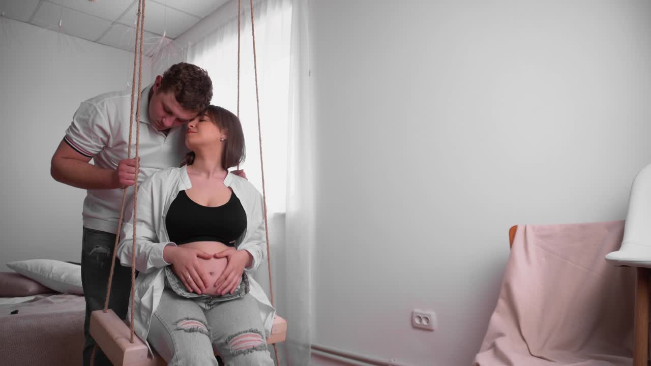 беременная молодая женщина с мужем, ожидающим ребенка. молодая семья ждет пополнения. счастливая беременная женщина с большим животом отдыхает дома. молодая будущая мать ласкает ее живот.