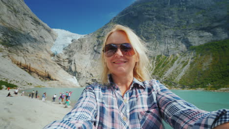 a happy woman is shooting a selfie video on a background of mountains and a glacier on top journey t