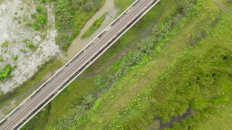 a spiral aerial footage towards the left revealing an elevated railway, farmland and marshland, muak klek, saraburi, thailand