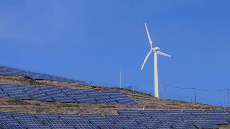 wind energy converter turbine blowing on top of a mountain full of solar panels alternative green enviomental energy