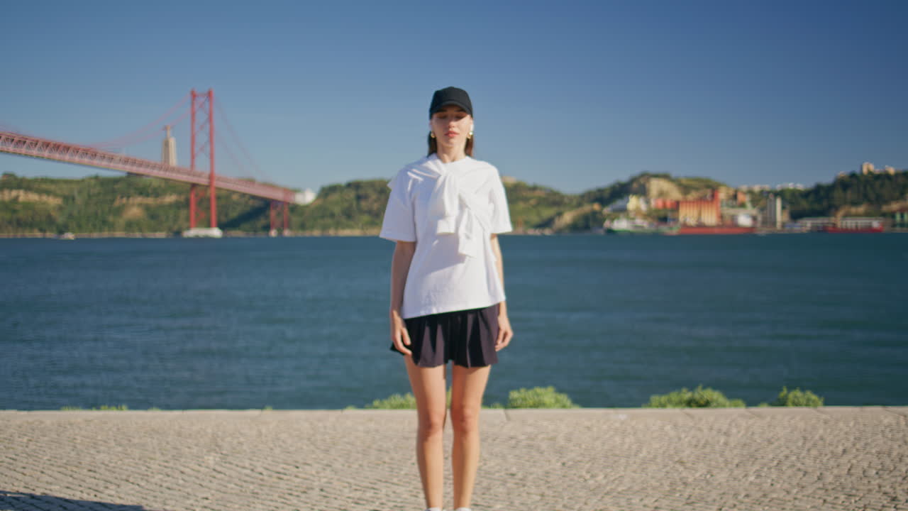 Stylish lady stretching body at sunny riverbank wearing cap. Active sportswoman
