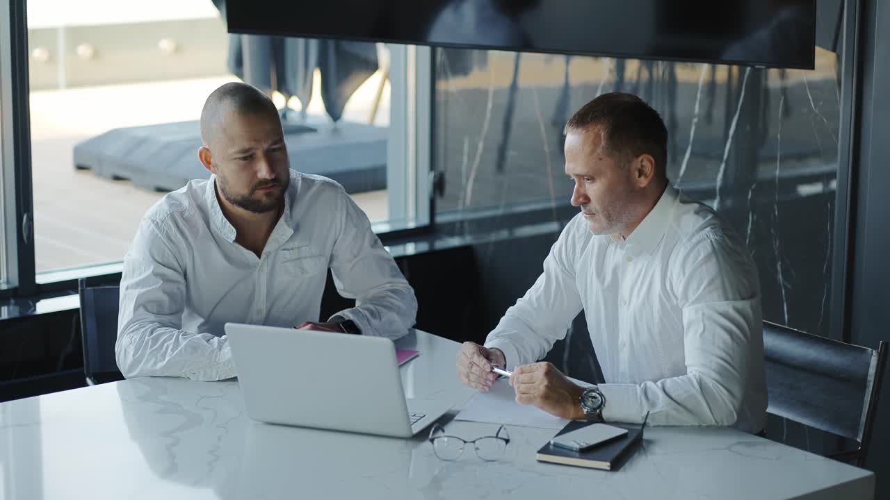 Due uomini d'affari che discutono i dati del mercato finanziario utilizzando un laptop e un tablet. Consulente finanziario, broker, manager.