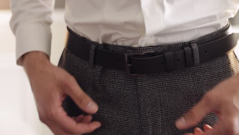 Groom-wears-belt,-man-in-white-shirt-puts-belt-on-pants-in-wedding-morning,-businessman-preparation