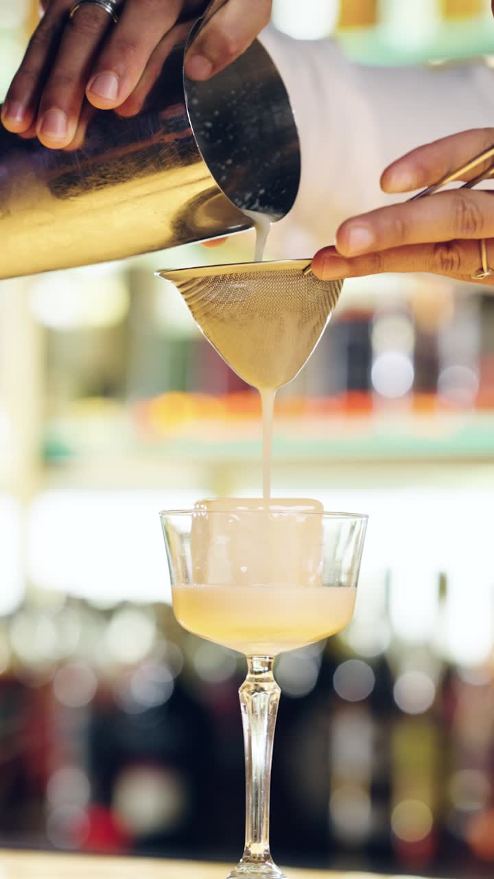 Barman che versa un cocktail attraverso un colino in un bicchiere con ghiaccio