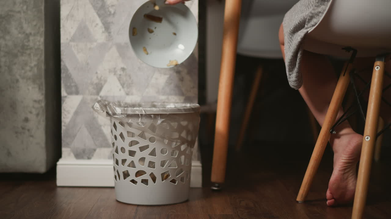 Person throwing food scraps into a trash can