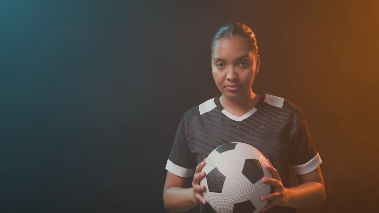 Donna afroamericana con una maglia nera che sistema un pallone da calcio, alzando lo sguardo per una posa sotto luce di contorno