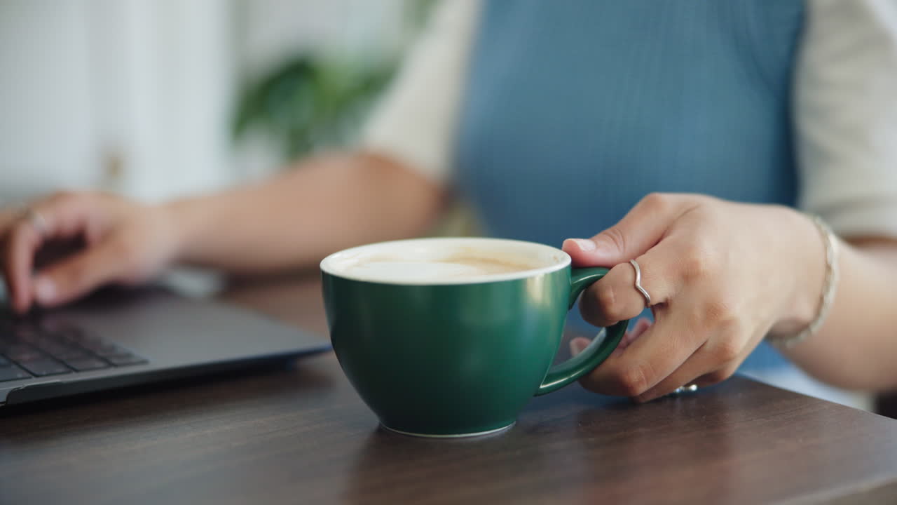 Donna che digita sul laptop e beve caffè alla scrivania