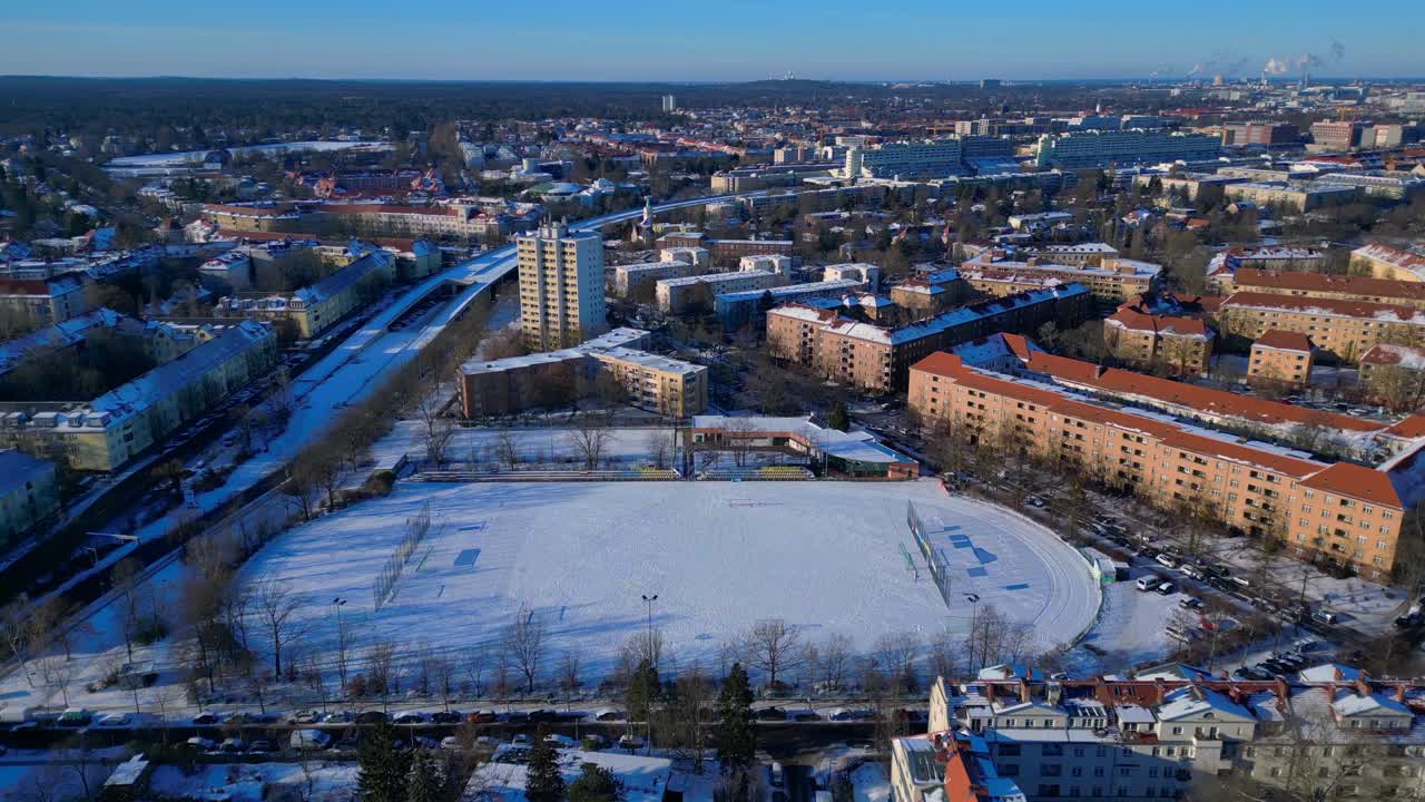 Saksan pääkaupungin maisema, jossa on lumen peittämä jalkapallokenttä ja juoksurata asuinrakennusten ympäröimänä talvella. Paras ilmakuvakulma, lennä eteenpäin, drone