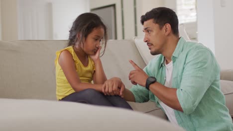 Hispanic-father-telling-off-his-young-upset-daughter-sitting-on-sofa