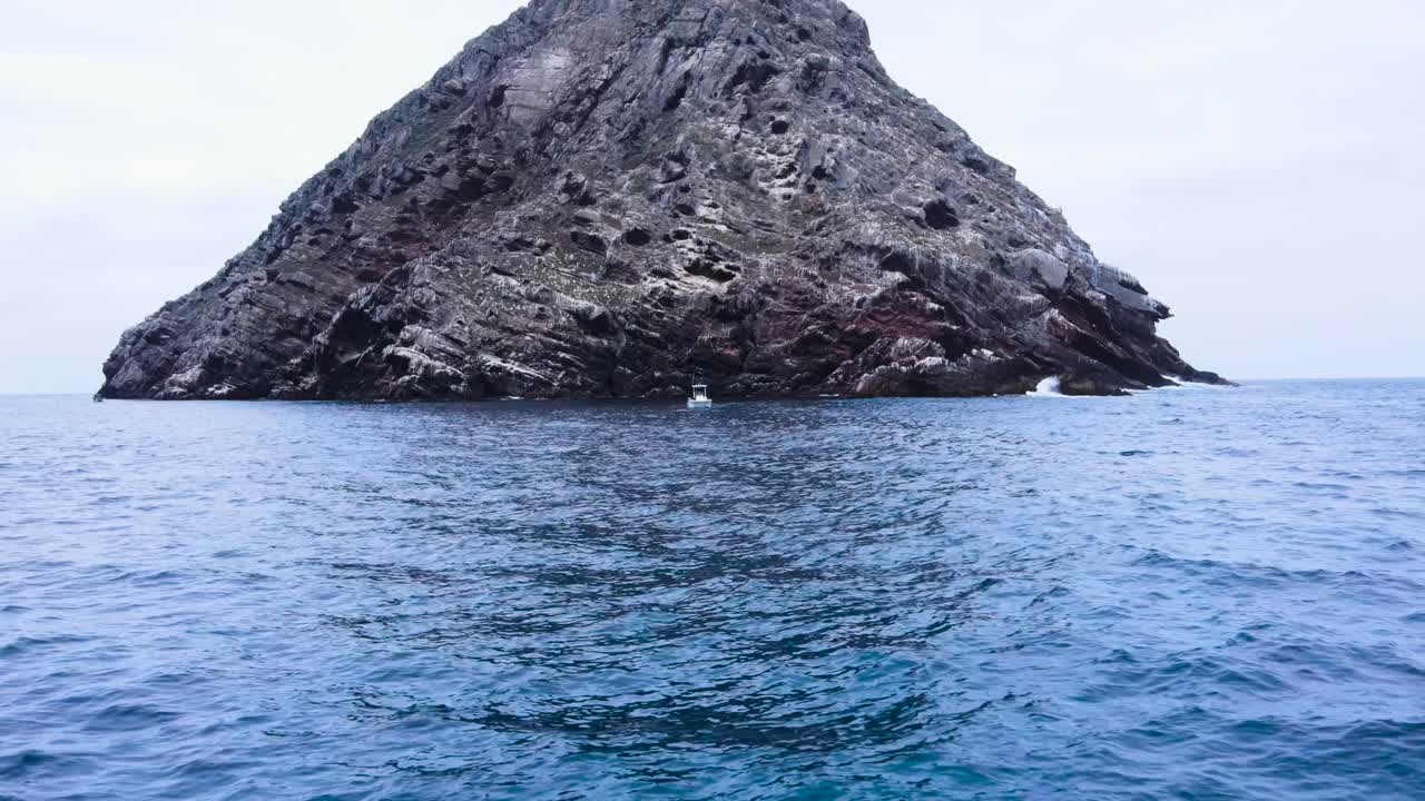Aerial pullback from boat anchored below rocky island in Coronado Islands, Mexico, surrounded by the vast blue ocean, centered fishing trip
