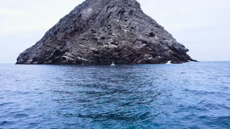 aerial pullback from boat anchored below rocky island in coronado islands, mexico, surrounded by the vast blue ocean, centered fishing trip