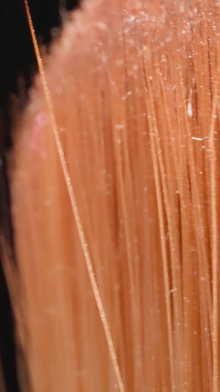 Orange bristles of used cosmetic brush with glitter on top for eye makeup. Professional product for applying eyeshadows on black background macro
