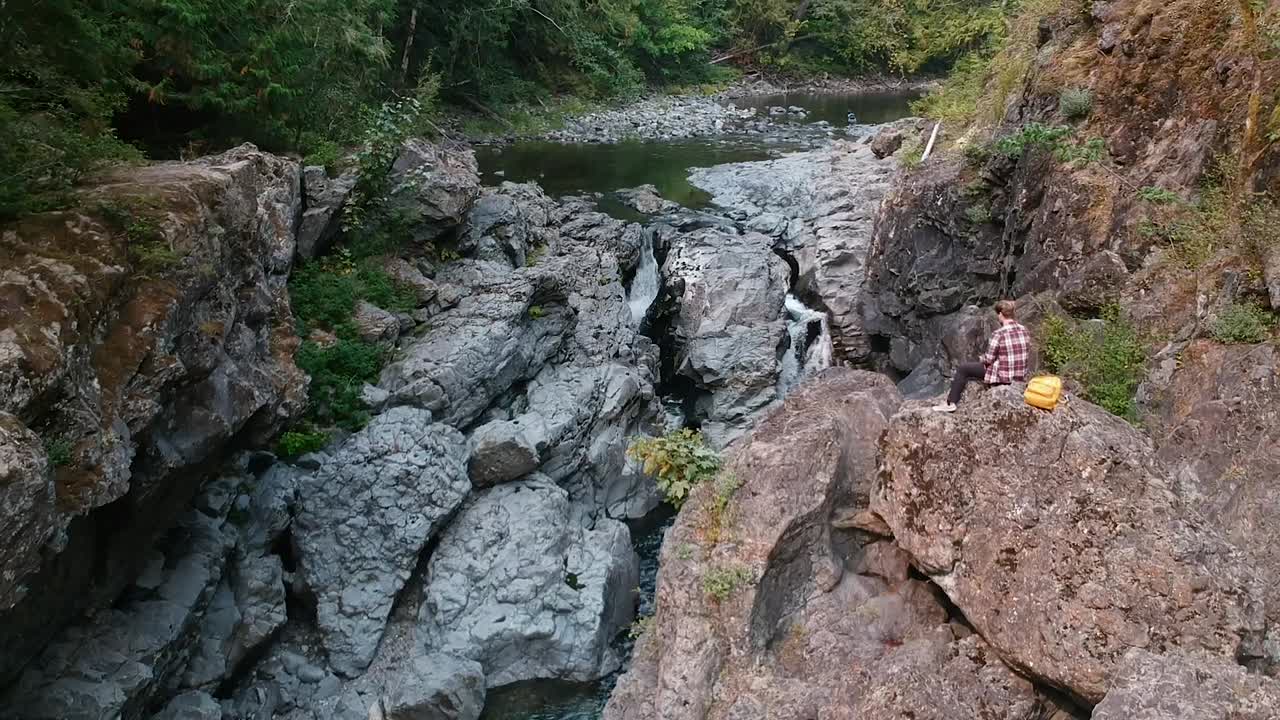 seguimiento de la toma de dos pequeñas cascadas con un hombre sentado en una roca con vistas a la hermosa escena en el campo de columbia británica, canadá