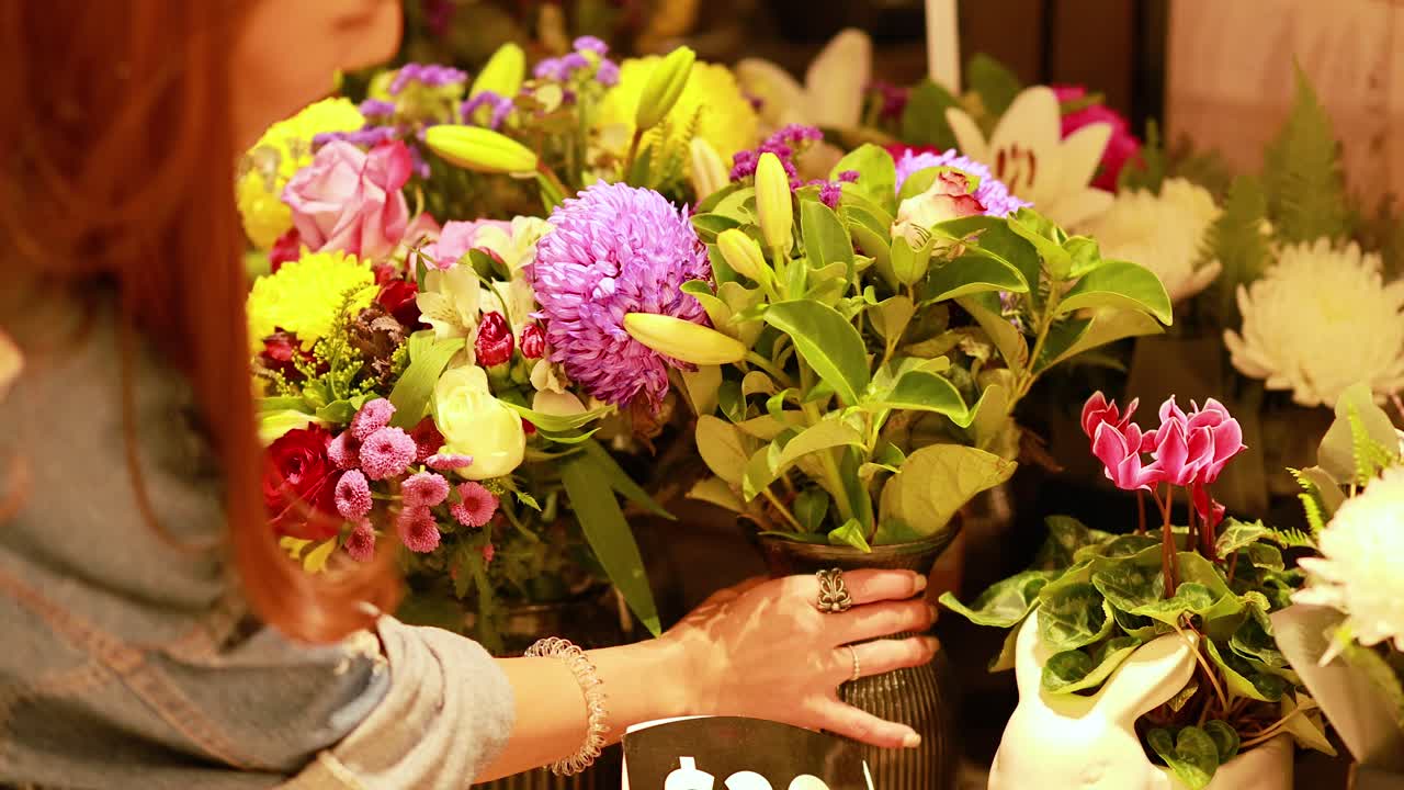 A person arranges vibrant flower bouquets in a warmly lit flower shop, creating a lively and colorful atmosphere