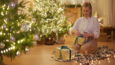 happy lovely woman by decorated christmas tree wrapping christmas presents