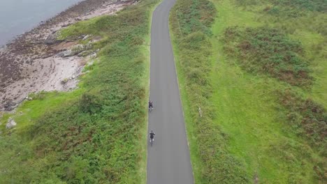 dos personas andando en bicicleta y deteniéndose en la carretera entre los prados verdes, escocia en un día nublado