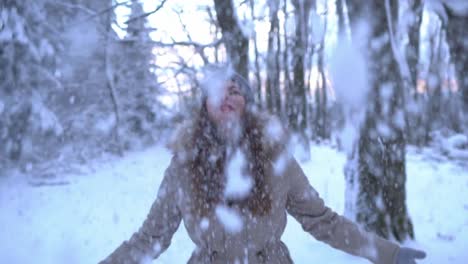 hermosa chica caucásica tirando nieve en el aire en el bosque de invierno, slomo