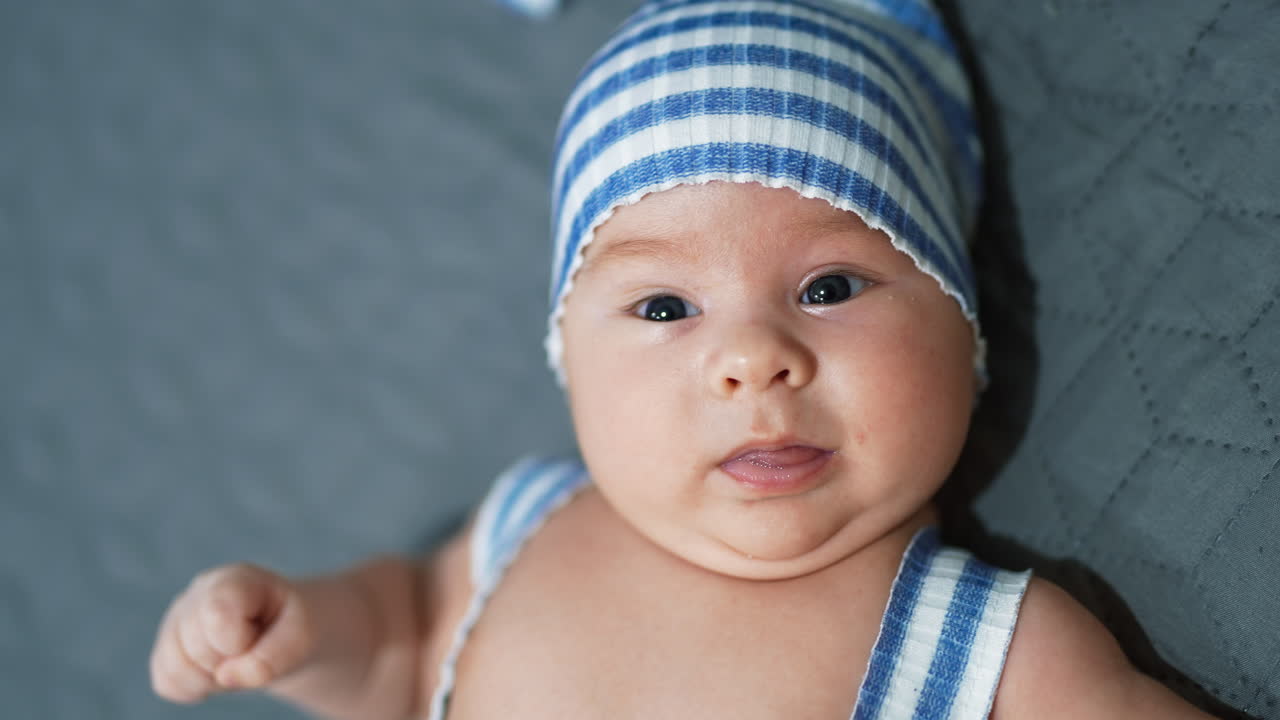 Cute toddler in adorable blue hat. Baby boy with plump cheeks at the grey backdrop. Face close up.