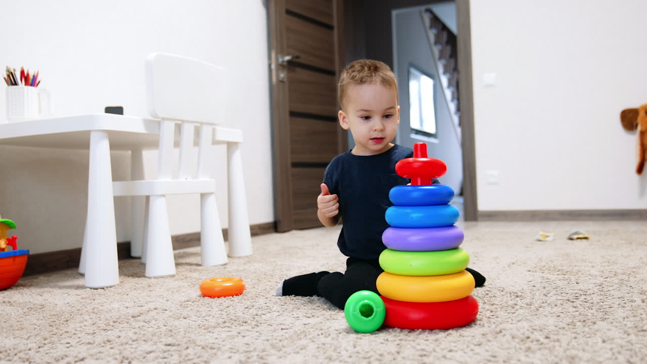 Beautiful Caucasian toddler sitting behind toy pyramid. Little kid playing at home sitting on the floor.