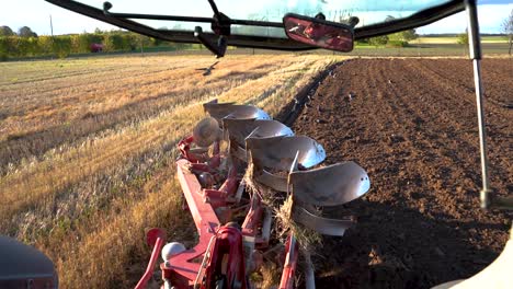 Birds-landing-on-freshly-plowed-field-behind-plow,-view-from-tractor-cabin